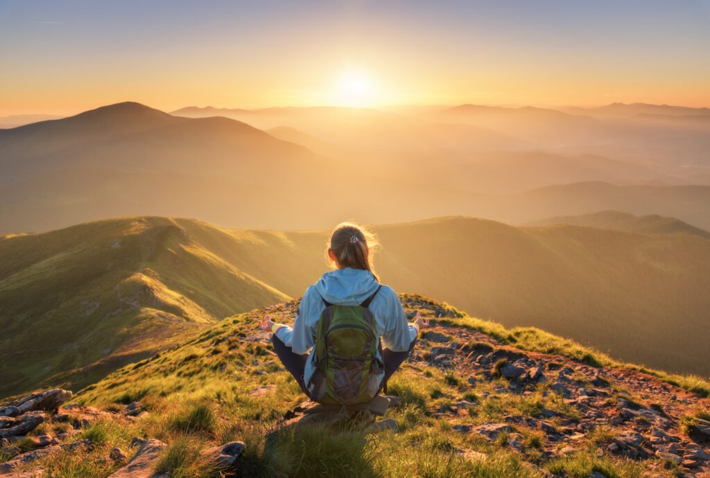 Young woman with backpack sitting on the mountain peak